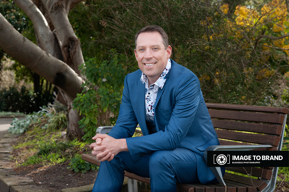 Photograph of a male sitting on a park bench in Geelong having his headshot taken by Image to Brand Photography.